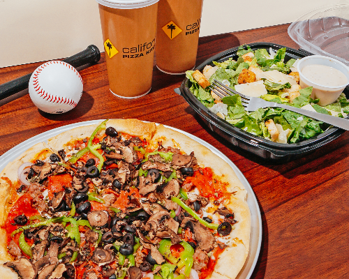 a pizza and salad with two drinks and a baseball on a table at California Pizza Kitchen